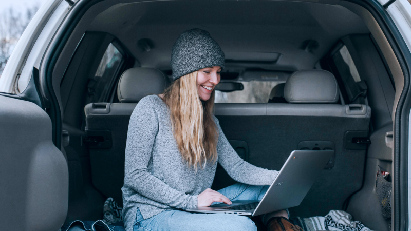 Eine Frau, die mit ihrem Laptop im Kofferraum ihres Vans sitzt.